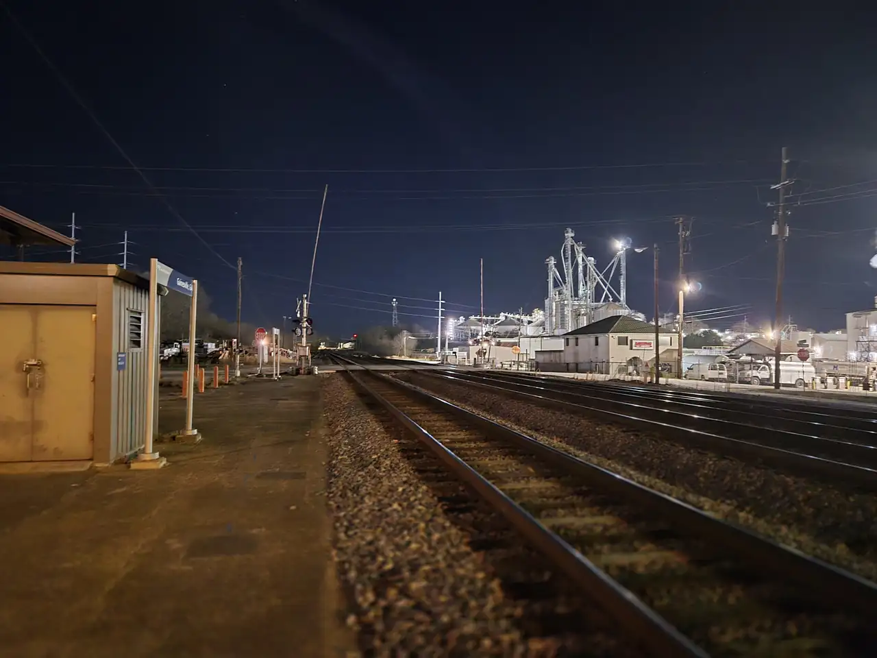 Night view along the rail line from the Gainesville Amtrak platform, three tracks running toward lit industrial buildings