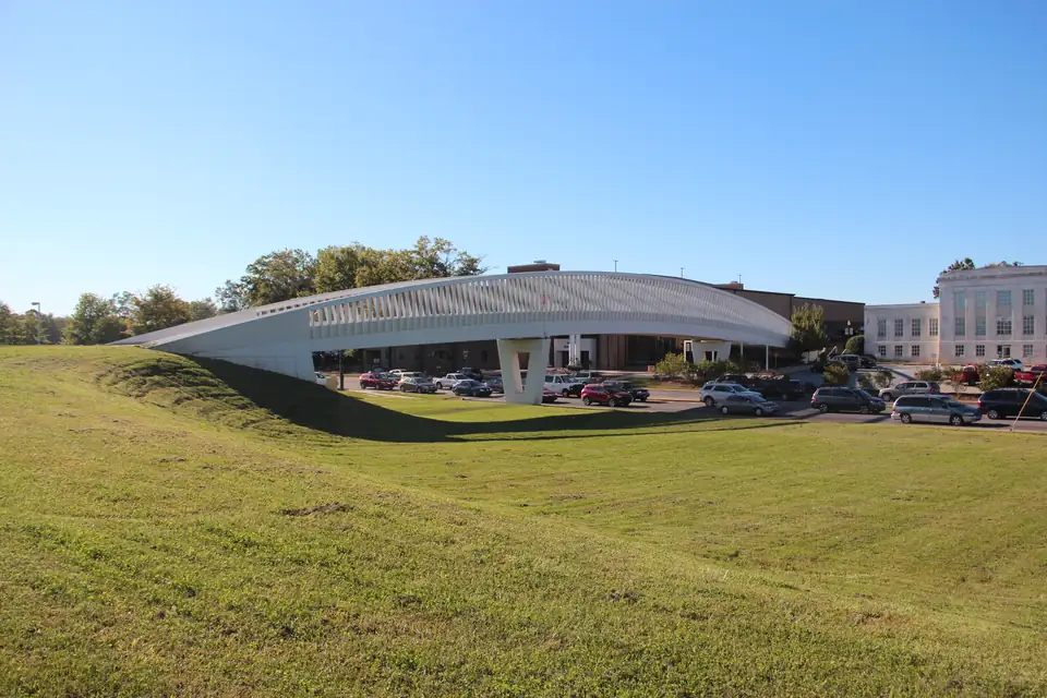 A covered pedestrian bridge crossing a downtown Gainesville parkway beside a grassy slope